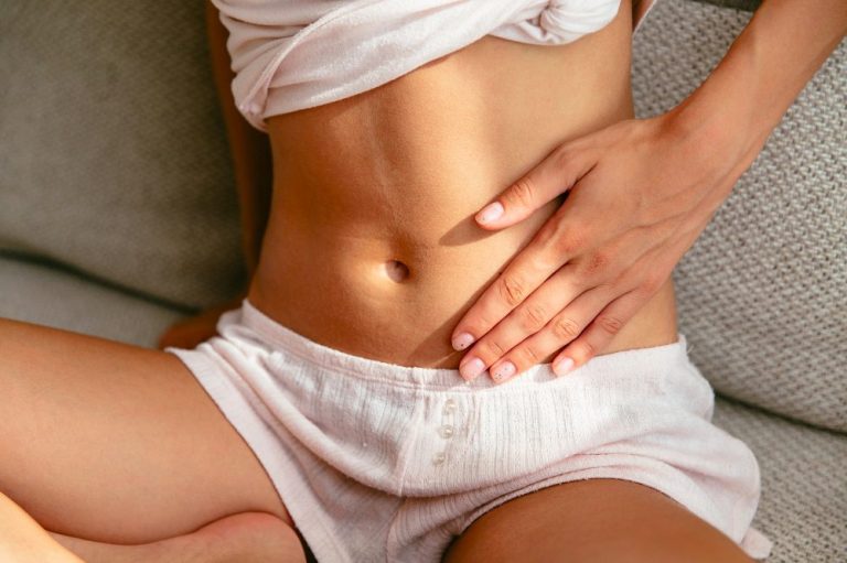 Eine Frau sitzt und hält sich mit einer Hand an den Bauch.