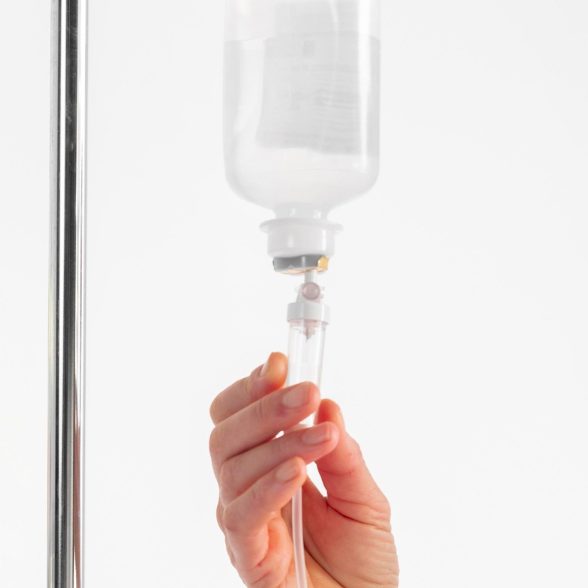 Eine Hand hält eine Infusionsflasche an einem Ständer für eine Vitalstoff Infusion.