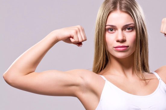 Junge Frau zeigt gestärkte Arme und wirkt selbstbewusst.